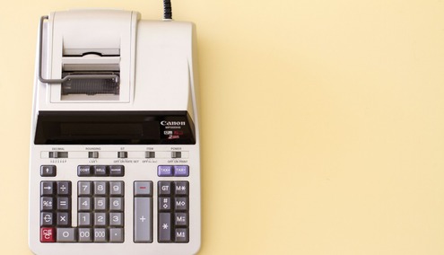 Une calculatrice imprimante Canon équipée d'un rouleau de papier et compatible avec Exact WinBooks est posée sur une surface jaune clair, vue d'en haut.